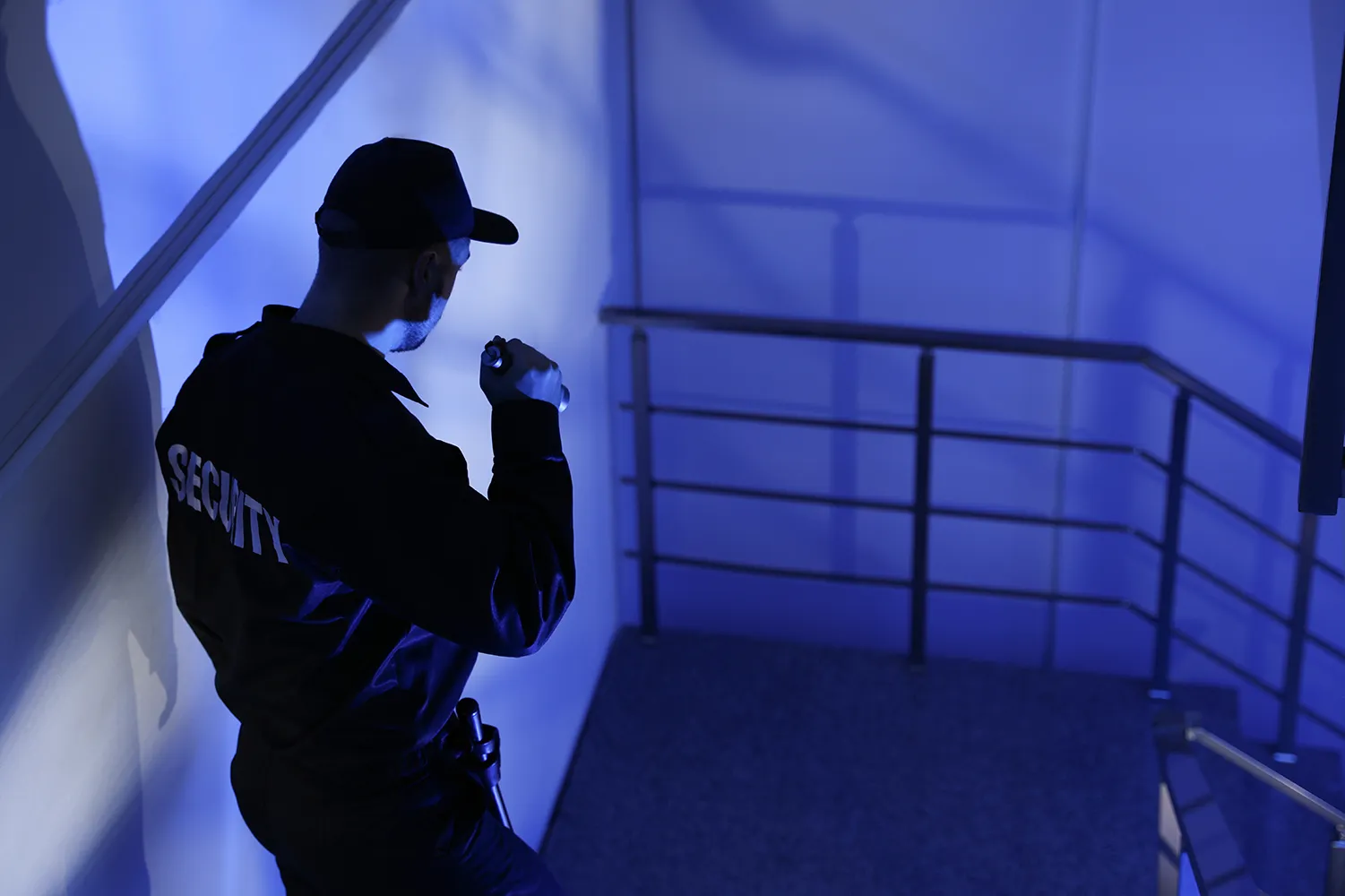 Männlicher Wachmann mit Taschenlampe auf einer Treppe in der Dunkelheit